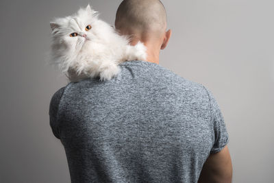 Rear view of man carrying cat against gray background