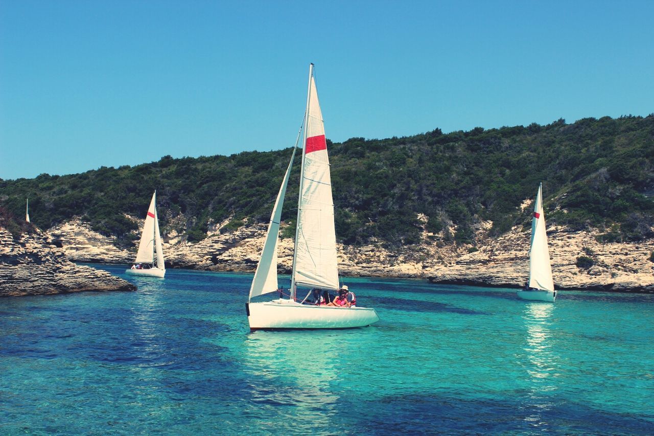 water, blue, clear sky, transportation, nautical vessel, waterfront, sea, sailboat, tranquility, tranquil scene, boat, mode of transport, nature, scenics, sailing, travel, flag, tree, beauty in nature, day