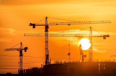 Low angle view of silhouette cranes against sky during sunset