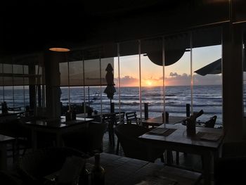 Silhouette of restaurant by sea against sky during sunset