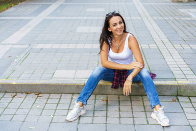 Outdoors lifestyle fashion portrait of contented young woman sitting outdoors.