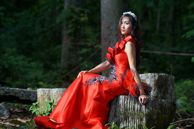 Portrait of fashionable young woman sitting on tree stump in forest