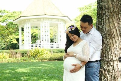 Portrait of smiling young man with daughter standing against trees