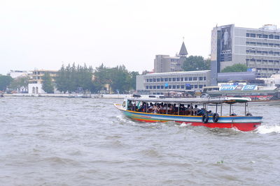 Boats in river by cityscape against clear sky