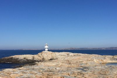 Lighthouse by sea against clear blue sky