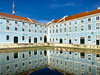 Buildings by river against blue sky in city