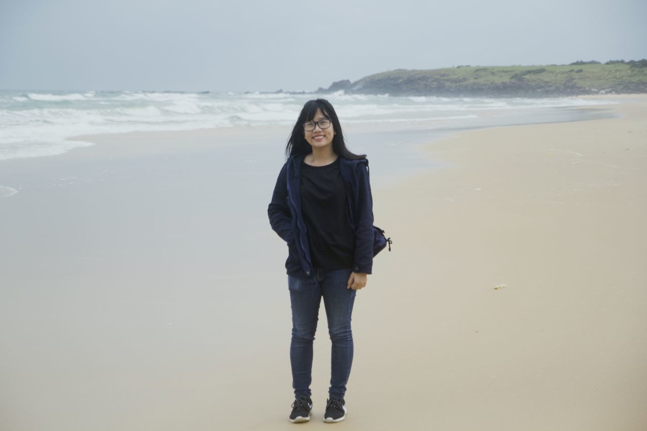 beach, sea, looking at camera, portrait, one person, three quarter length, beauty, standing, horizon over water, one woman only, real people, beautiful woman, leisure activity, front view, smiling, sand, wave, vacations, only women, day, nature, happiness, people, sky, water, young adult, outdoors, adults only, beauty in nature, young women, adult, one young woman only