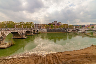 Arch bridge over river against sky in city