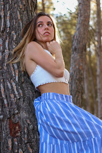 Side view portrait of a brunette woman leaning against a tree looking back wearing a boho outfit