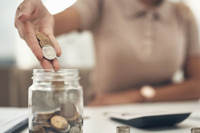 Midsection of woman pouring coins in jar