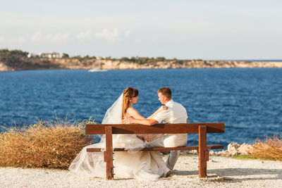 Couple sitting by sea against sky