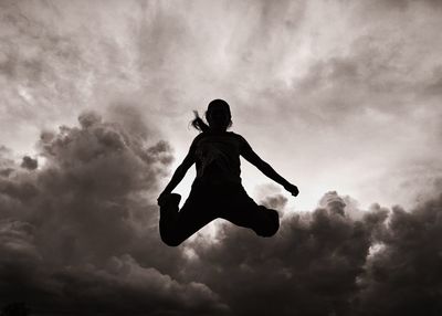 Silhouette woman jumping in mid-air against cloudy sky