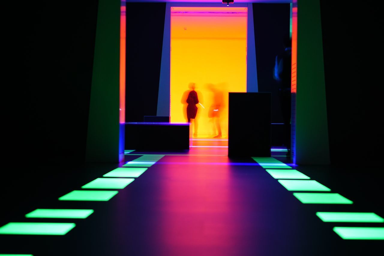 REAR VIEW OF MAN STANDING AT ENTRANCE OF ILLUMINATED BUILDING