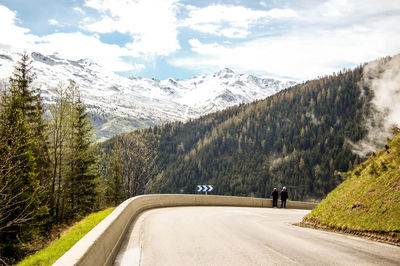 Road amidst trees and mountains against sky