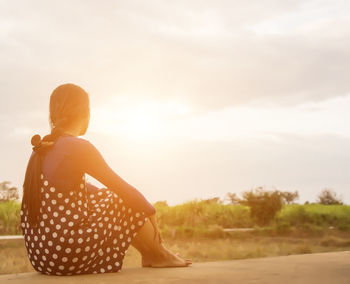 Rear view of woman sitting on land against sky