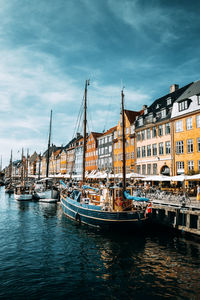 Boats moored in canal by buildings against sky