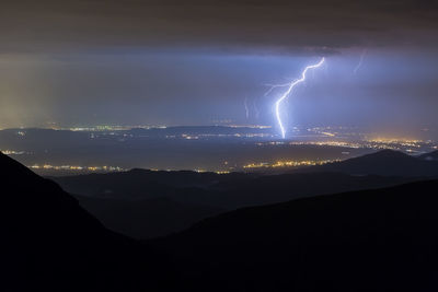 Panoramic view of lightning over mountains against sky at night