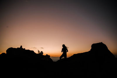 Silhouette people standing on rock against sky during sunset