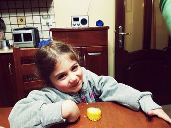 Smiling cute girl having sweetcorn while sitting at wooden dining table in kitchen