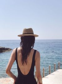 Rear view of young woman standing at beach against clear sky