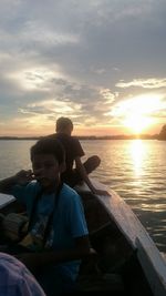 Rear view of friends sitting on boat against sky during sunset