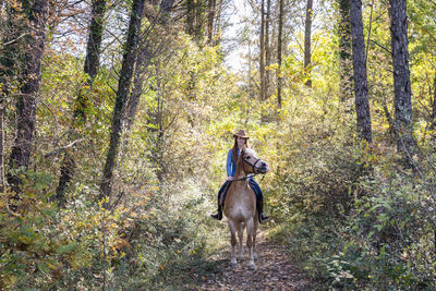 Young woman horseback riding amidst plants and trees