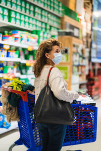 Side view of woman wearing mask standing at shopping mall