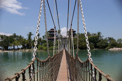 Rope bridge over river against blue sky