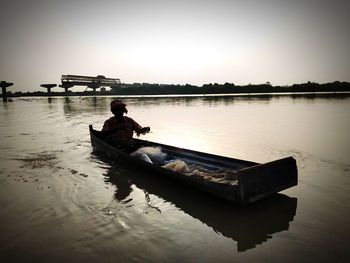 Man sitting on boat in lake against sky