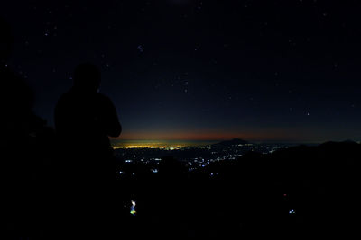 Silhouette people at illuminated city against sky at night