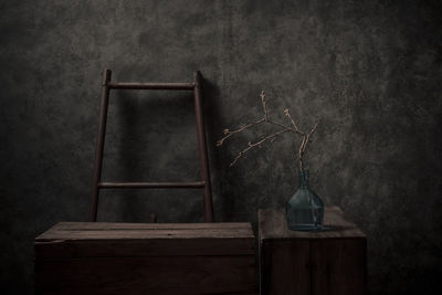 Dry plant in vase by ladder against wall