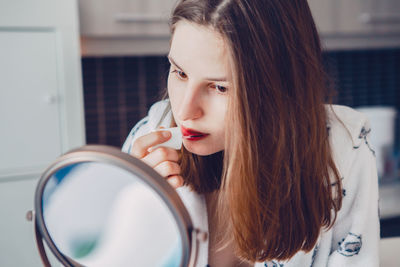 Close-up of woman applying lipstick while looking in mirror