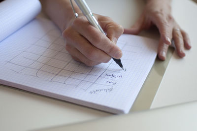 Cropped hand of businesswoman writing on book while working in office