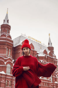 Woman in a red warm sweater and hat in winter stands on a moscow street a red building 