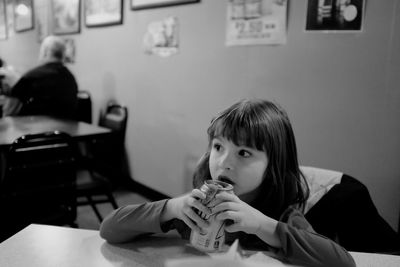 Cute girl drinking drink while sitting on chair at restaurant