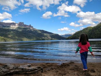 Rear view of man standing by lake against sky