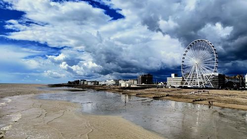 Ferris wheel at beach against cloudy sky