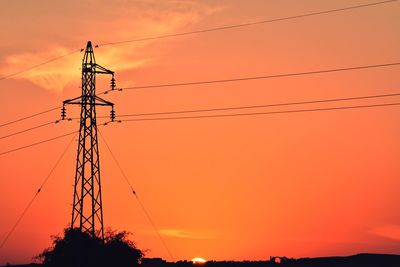 Low angle view of silhouette electricity pylon against orange sky