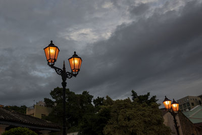 Low angle view of illuminated street light by building against sky