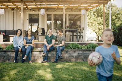 Smiling homosexual parents looking at son holding soccer ball in backyard