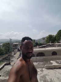 Portrait of shirtless man standing in swimming pool against sky