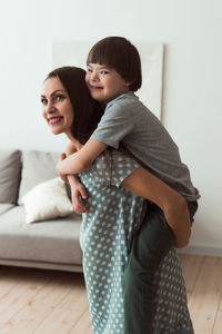 Smiling mother carrying son piggyback at home