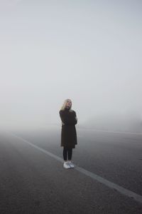 Full length of young woman standing on road in foggy weather