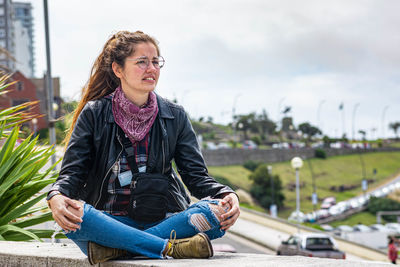 Young woman sitting on surrounding wall