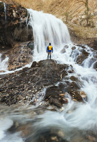 Rear view of man standing on rocks by waterfall