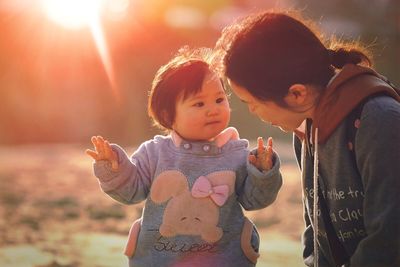 Mother looking at cute daughter standing in park during sunset