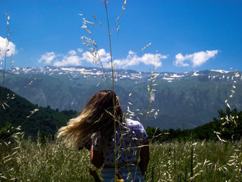 Rear view of woman standing on field against mountains and sky