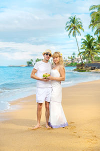 Portrait of couple holding coconut at beach on vacation