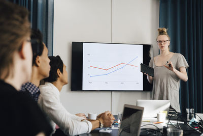 Confident genderblend businessman explaining strategy over graph to colleagues in board room during meeting