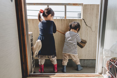 Side view of mother and daughter standing by window